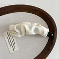 Nahaufnahme der cremefarbenen Bananenspange aus Satin mit goldenem Metalldetail - Gebrochenes Weiß