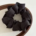 Detail of a black pleated scrunchie with ruffled edges on a wooden tray with linen - Black