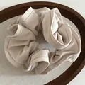 Detailed texture of a soft beige fabric scrunchie with ruffled edges on a wooden tray - Beige