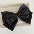 Detail of multi-layered large black satin bow clip on a beige linen display tray - Black