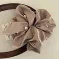 Close-up of champagne satin scrunchie with faux pearls and silver rivets detail - Khaki