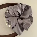 Close-up of grey satin scrunchie with silver studs and white pearls on wood tray - Light Gray