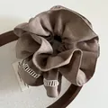 Detail of khaki linen scrunchie featuring delicate white hollow-out lace embroidery edges - Brown