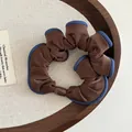 Braunes und blaues Satin-Haargummi mit Kontrastrand auf einem dekorativen Holztablett - Braun