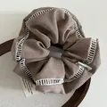Brown fabric scrunchie with white lace trim and cute baby tag on wooden display base - Brown