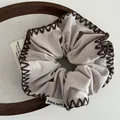 Close-up of light gray scrunchie with dark brown hand-stitched edges and cute baby tag - Apricot