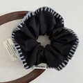 Detail of handcrafted black scrunchie with gray wool blanket stitch edge on wood tray - Black