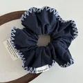 Detail of dark blue scrunchie with white hand-stitched edges and 'cute baby' woven label - Navy Blue