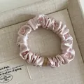 Close-up of pale pink satin hair scrunchie with transparent pink crystal beads and fine pleats - Pink