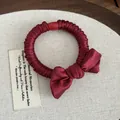 Close-up of burgundy pleated satin hair tie with a bow and red decorative bead - Red