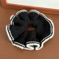 Chic black knitted scrunchie with white wave contrast trim on a rustic wooden background - Black