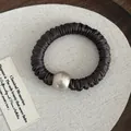 Detail of dark brown pleated satin hair scrunchie featuring a large metallic accent bead - Brown