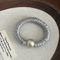Detail of grey satin pleated scrunchie featuring a large champagne pearl bead on wood - Blue Gray