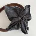 Détail d'un chouchou en maille gris foncé avec paillettes et étiquette Hand Made - Gris