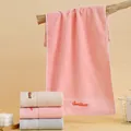 Pink cotton towel with Goodliness embroidery and wavy border shown hanging in bathroom - 74cmx34cm / Multicolor