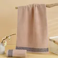 Thick light brown cotton towel with blue Greek key jacquard pattern on a wooden stand - Camel / 74x34cm