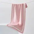 Soft pink coral fleece towel with white border hanging in a minimalist studio setup - 40x80cm / Sakura Pink