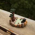 Black cat figurine in miniature hot spring with pine tree as a smartphone stand - Black Cat Hot Spring