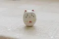 Miniature white ceramic Maneki Neko figurine with red fortune symbol on lace - White