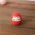 Figura Daruma japonesa de cerámica roja con detalles dorados sobre mesa de madera - Rojo