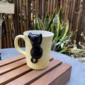 Pale yellow ceramic cat mug with a 3D black kitten figurine and textured vertical stripes - Cream Black Cat