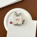 Cartoon Acrylclip weiße Katze mit roter Schleife und Kirsche auf Holztisch - Artige Katze
