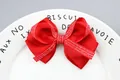 Macro detail of red grosgrain ribbon bow with cursive white lettering on a ceramic plate - Red