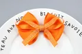 Orange grosgrain ribbon hair bow with white script lettering on a ceramic plate background - Orange