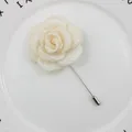 Close-up of a cream fabric rose brooch with long silver metal pin on a white ceramic plate - Beige