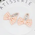 Close-up of two girls' orange houndstooth bow hair clips on a white ceramic plate - Pink
