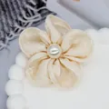 Vue macro d'un accessoire floral en organza crème avec détail de perle centrale - Base plate / Beige