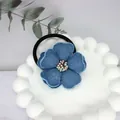 Close-up of blue denim camellia flower hair tie with beaded center on a white tray - Flower Core Style / 5cm / Sky Blue Denim