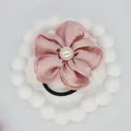 Detailed view of dusty rose satin flower hair tie with central faux pearl on white tray - Pink