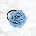 Close-up of denim fabric rose hair tie resting on white pebbles with elastic band detail - Rose Scrunchie / Denim Blue