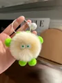 Detail of a fluffy cream monster keychain with green ears, big eyes and a white bell - Off White