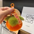 Dettaglio portachiavi a forma di cachi in peluche con clip arancione e ciondolo - Buone Notizie Successive