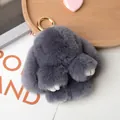 Cute grey fluffy rabbit fur keychain with gold metal ring on a warm wooden tray background - Dark Gray