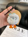 Close-up of grey plush monster keychain with blue ears held in hand over Vogue magazine - Gray