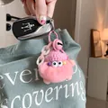 Detail of a pink plush monster keychain with fluffy faux fur and a knit hat on a blue bag - Pink