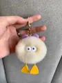 Close-up of white plush duck keychain with purple bow and golden metal lobster clasp - Off White