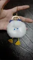 White rabbit fur duckling keychain with blue ears and gold metal clip on leather background - White