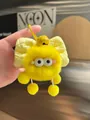 Detail of a yellow plush monster keychain with a checkered bow and bell on a bag - Yellow