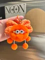 Close-up of bright orange plush monster keychain with bow and metal clip accessories - Orange