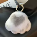Close-up of a white and grey plush cat paw pendant with a gold ring on a black bag - Light Gray