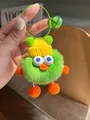 Macro detail of fuzzy green monster plush keychain with yellow knit hat and orange pom-poms - Green