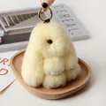 Fluffy beige faux fur rabbit charm with golden ring clip on a light wooden tray - Off White