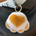 Detailed view of plush cat paw keychain with soft fur on a black leather handbag - Mango Yellow