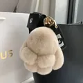 Plush bunny keychain in beige faux fur with golden metal clip on a black leather handbag - Milk Tea