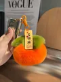 Dettaglio portachiavi a forma di cachi in peluche arancione con etichetta Good Luck e foglia - Buona Fortuna