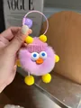 Detail eines lila Plüschmonster-Schlüsselanhängers mit rosa Strickmütze und Glocke - Hellviolett